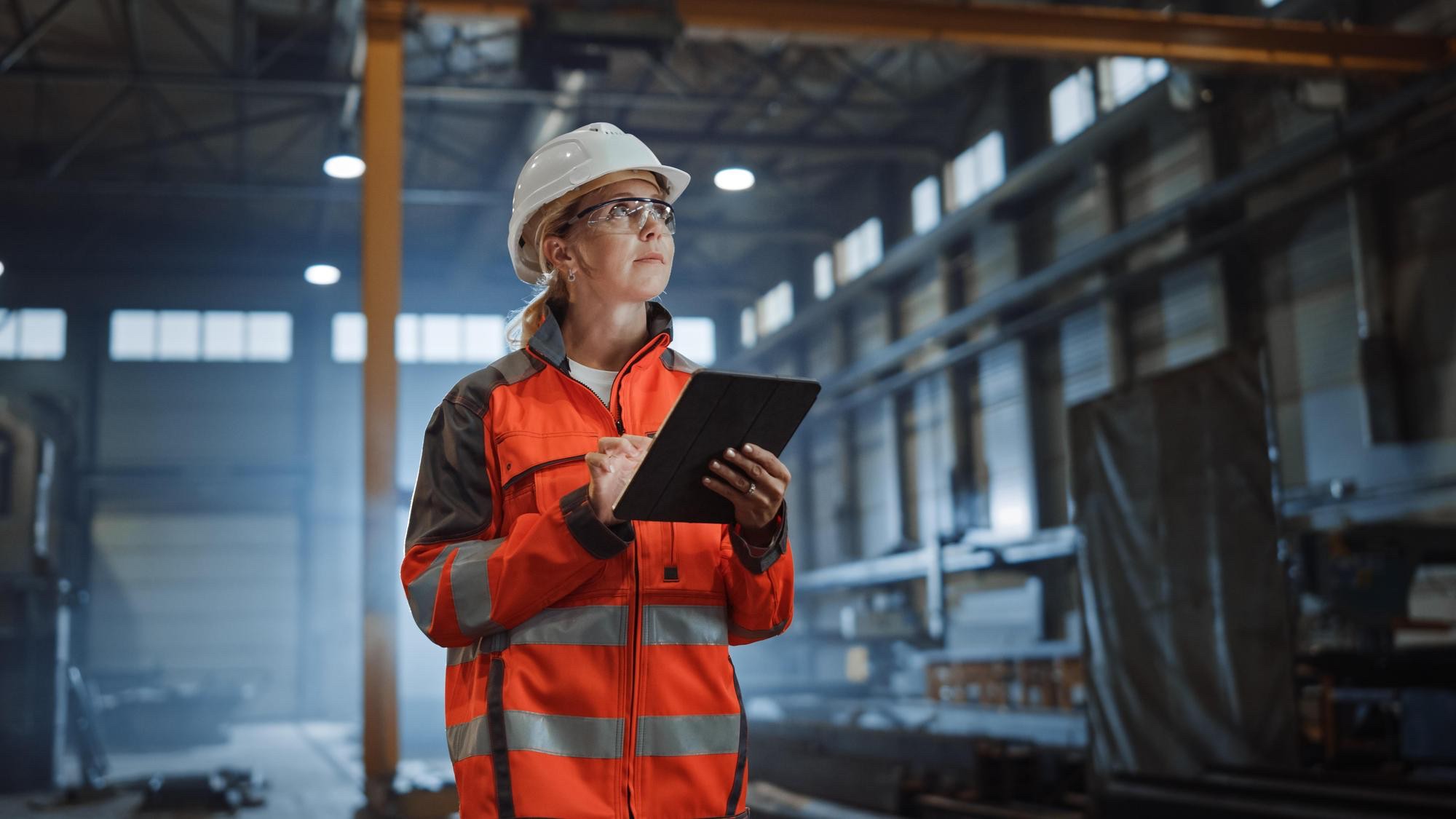 Industriemitarbeiterin bedient eine Anwendung auf dem Tablet in der Produktionshalle