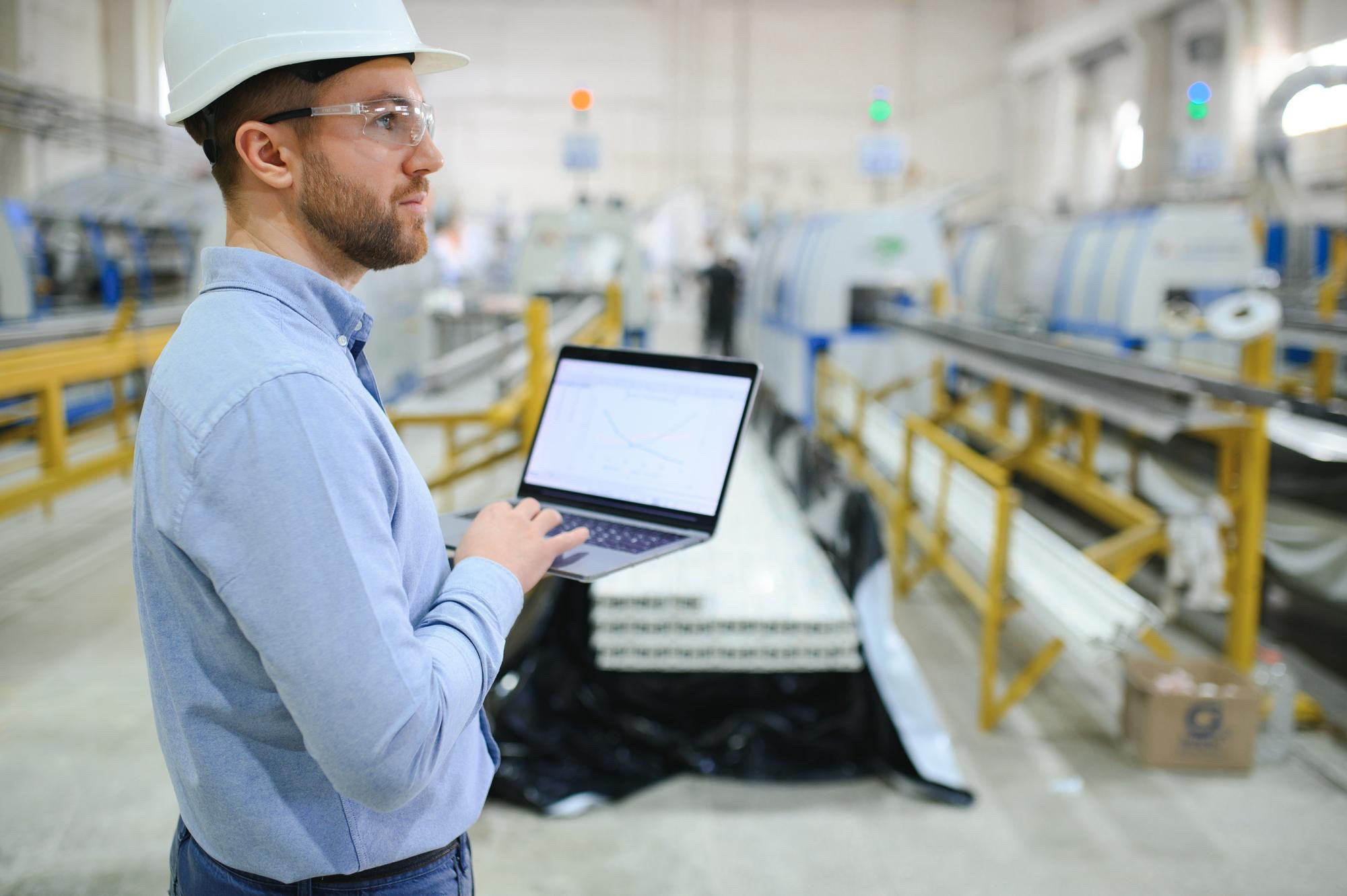 Techniker mit Laptop wertet Daten in einer Produktionshalle aus